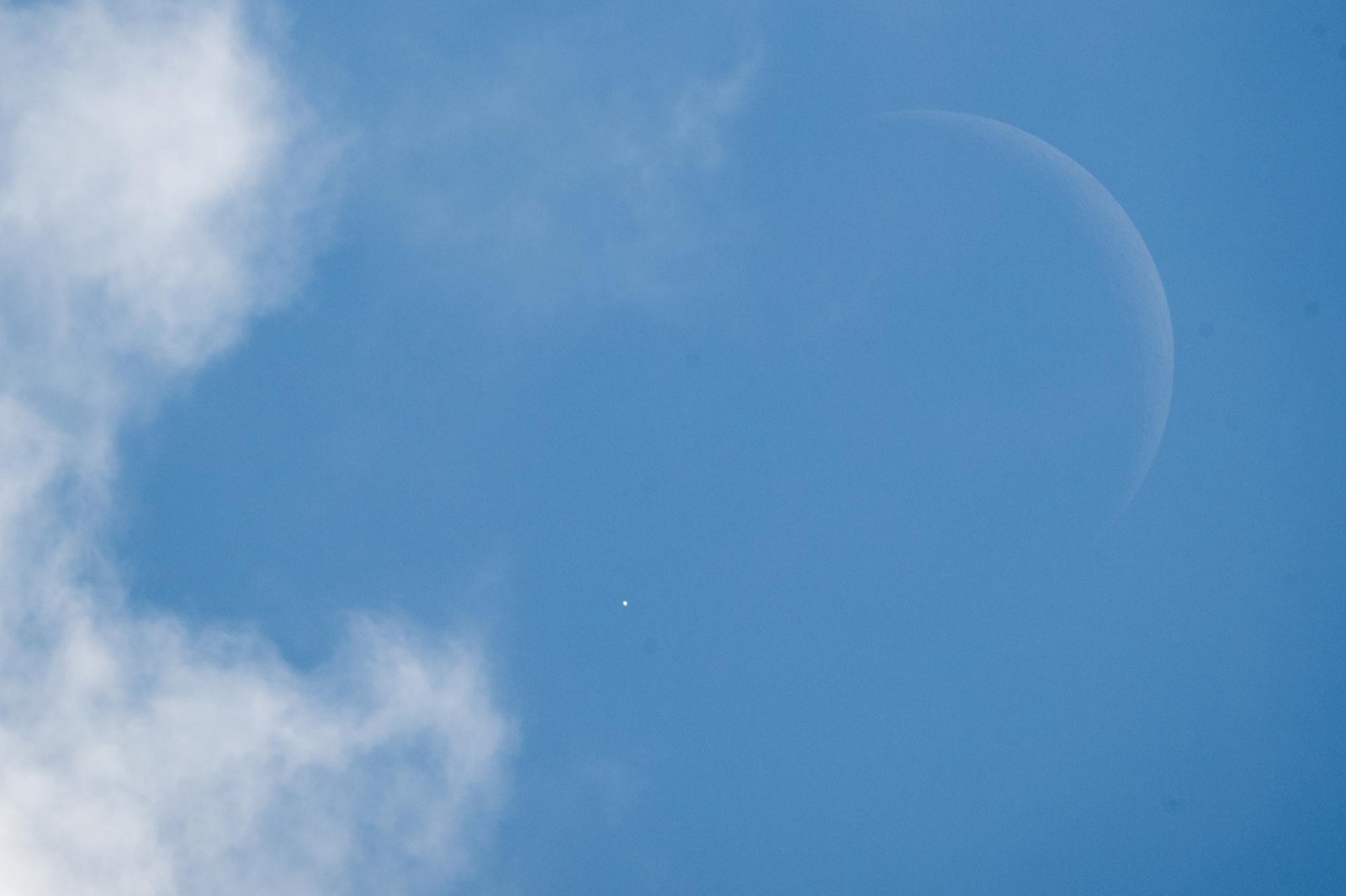Thin crescent Moon in a blue sky with a bright point of light at its edge and white cloud at left.