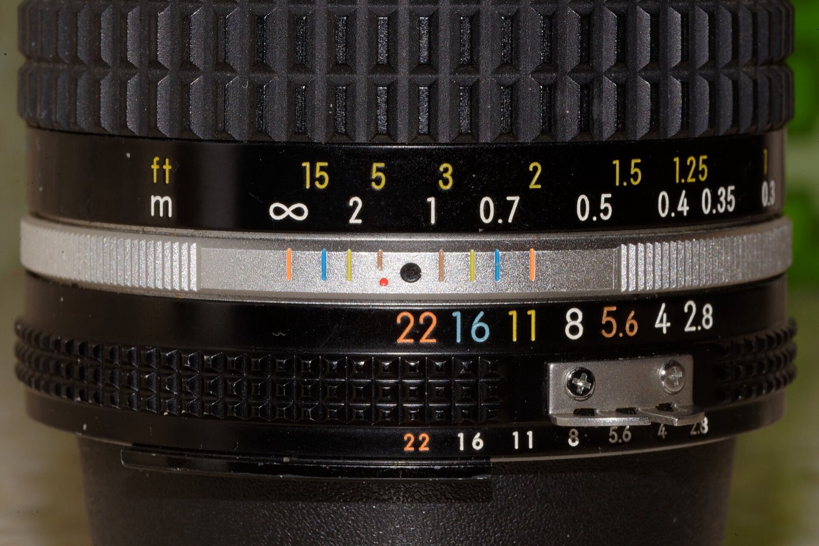 Close-up of a lens barrel with distance scale in feet and metres, infinity symbol and coloured aperture numbers.