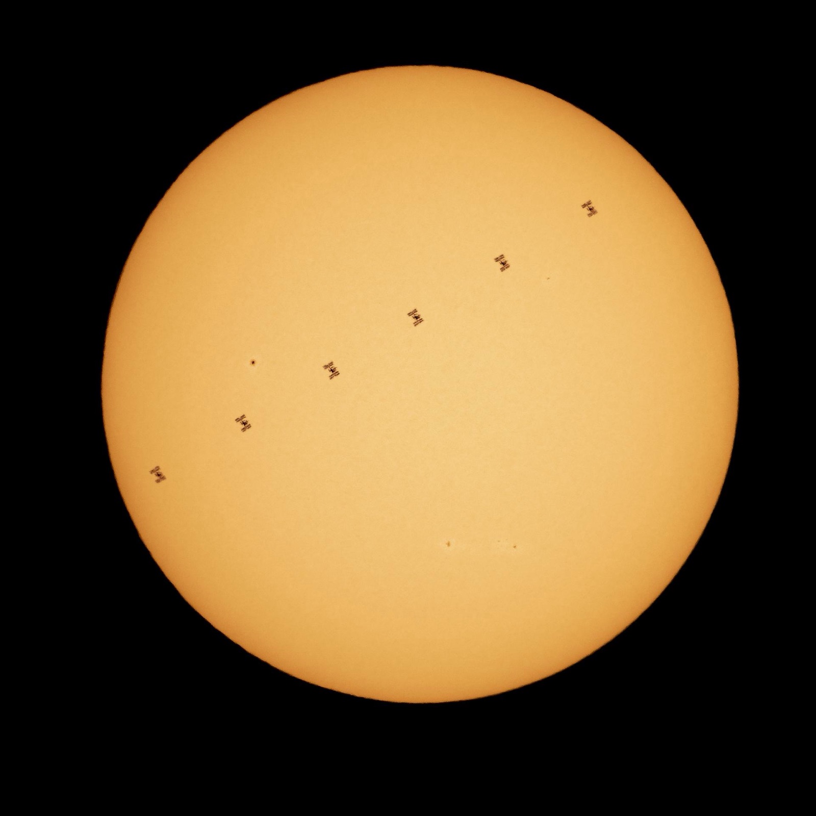 Orange solar disc with six small silhouettes of the space station in a line across it.