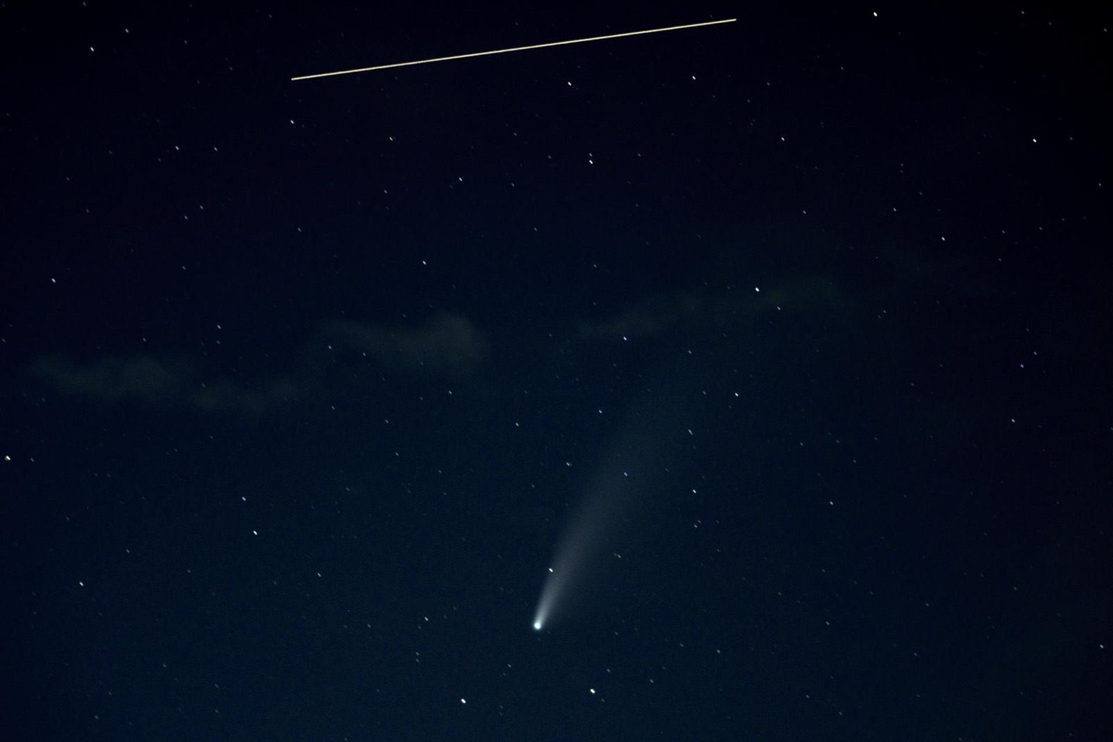 Short straight light trail of the space station above a comet with a tail in a dark blue sky.