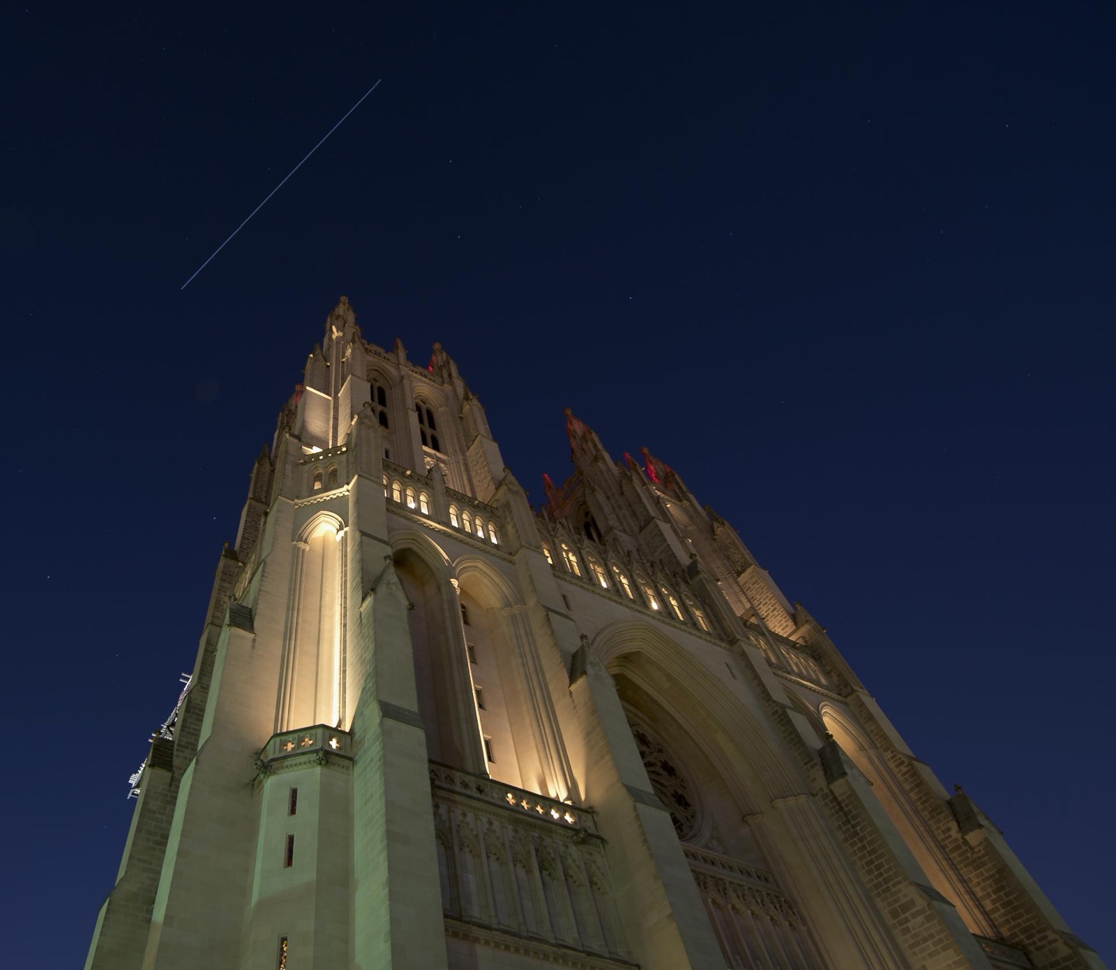 Light trail of the space station crossing a dark blue sky above a floodlit cathedral.
