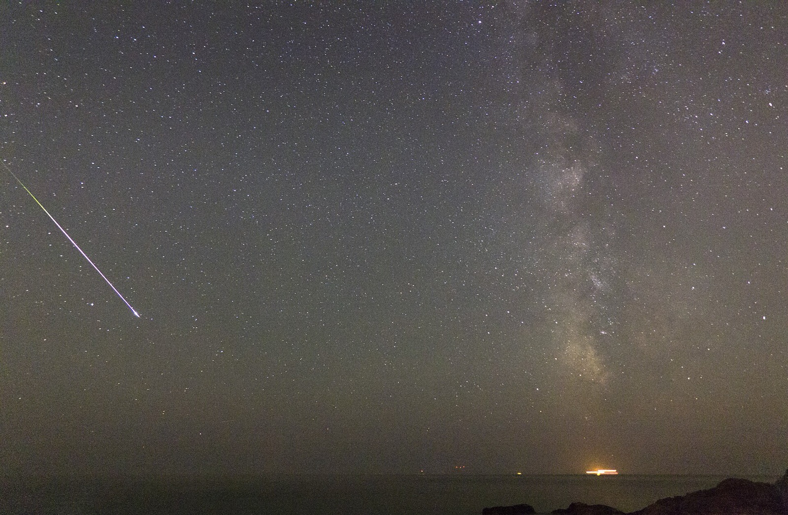 Bright meteor streak at left and the Milky Way at right over a dark sea horizon.