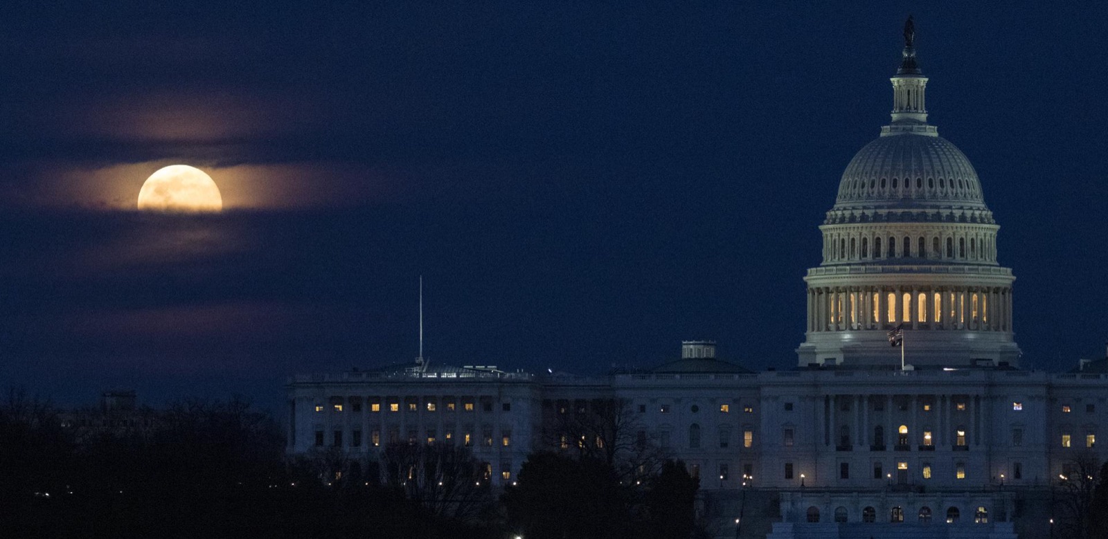 Full Moon rising behind the dome of the U.S. Capitol at dusk, partly veiled by thin cloud.