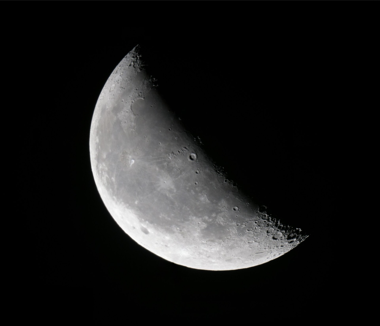 Waning crescent Moon on black with craters sharply shadowed along the line between light and dark.
