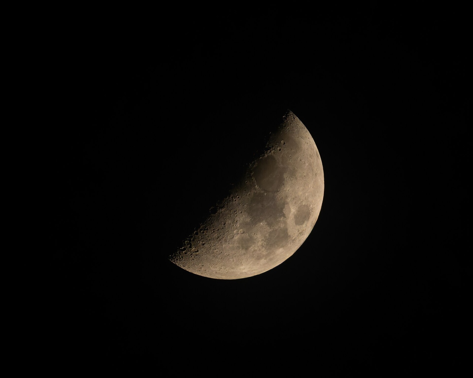 First-quarter Moon on a black sky with sharp craters along the line between light and dark.