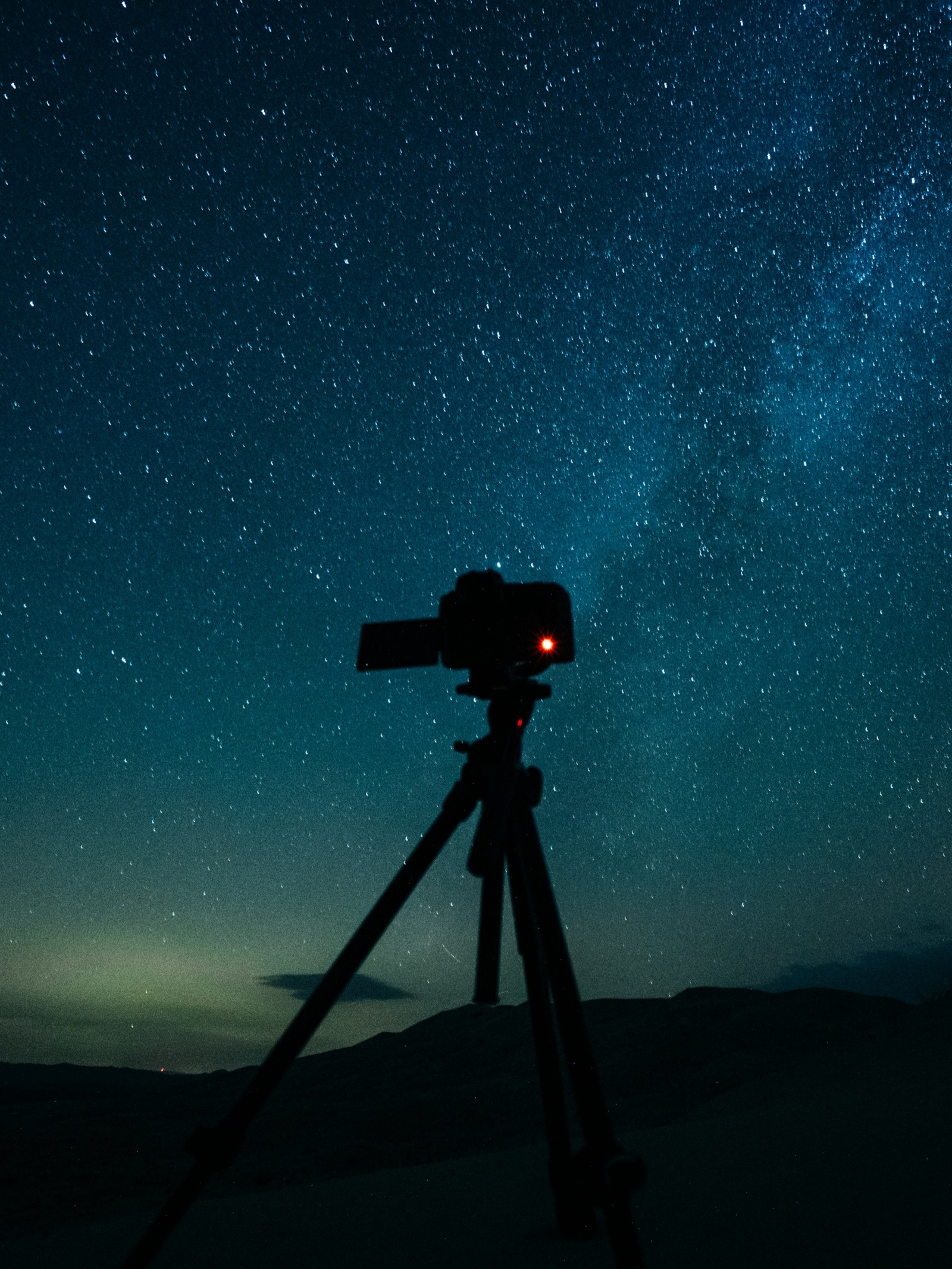 Silhouette of a camera on a tripod with a red light, under a starry sky