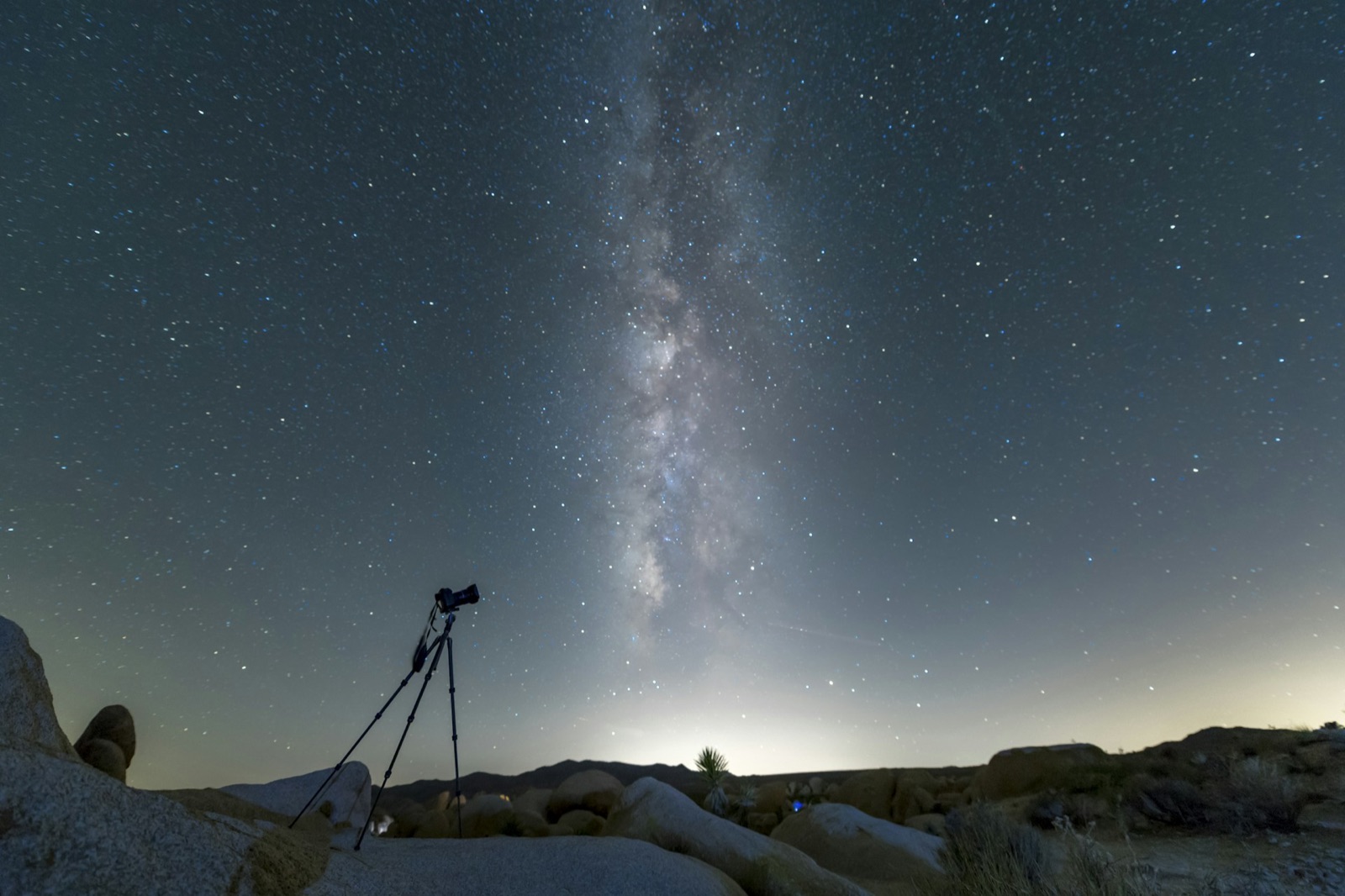 Tripod and camera silhouetted on desert rocks beneath the Milky Way