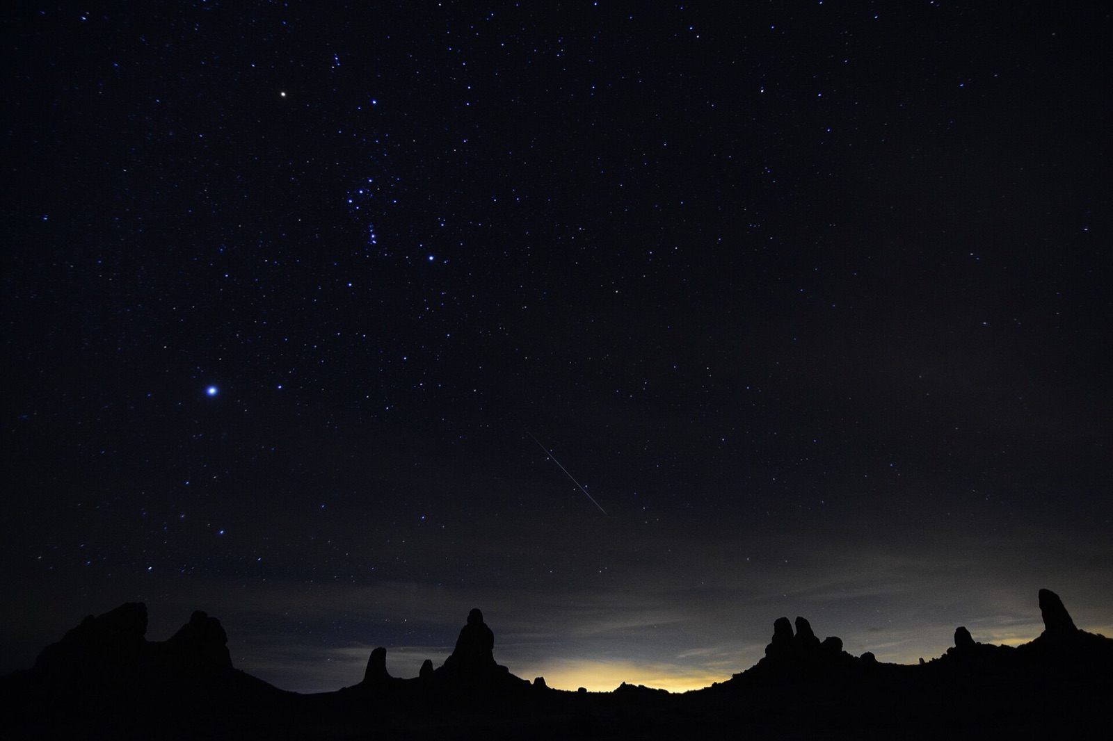 Meteor streak over desert rock spires under a starry sky