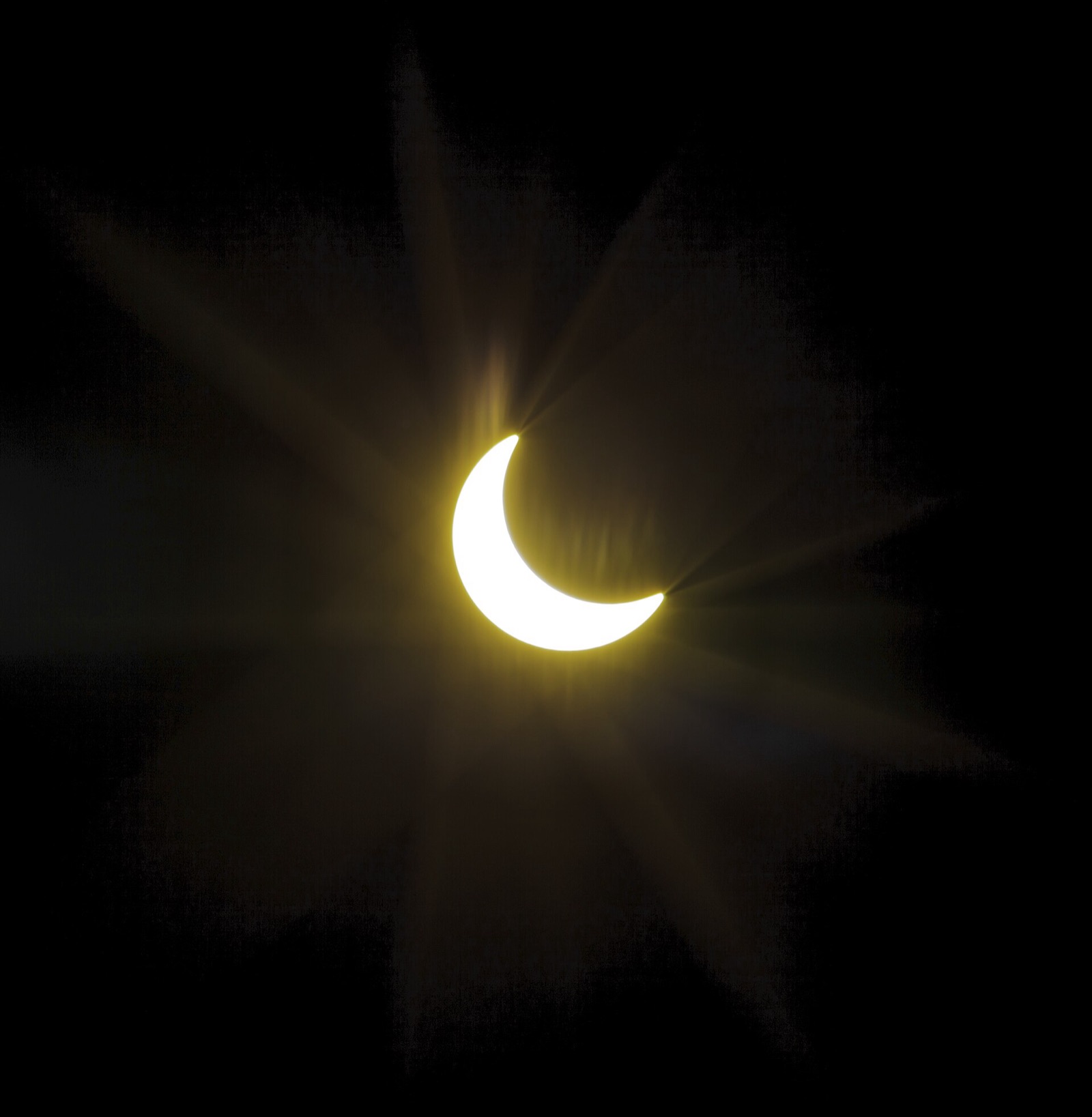 The Sun as a thin bright crescent against a black sky during a partial eclipse phase.