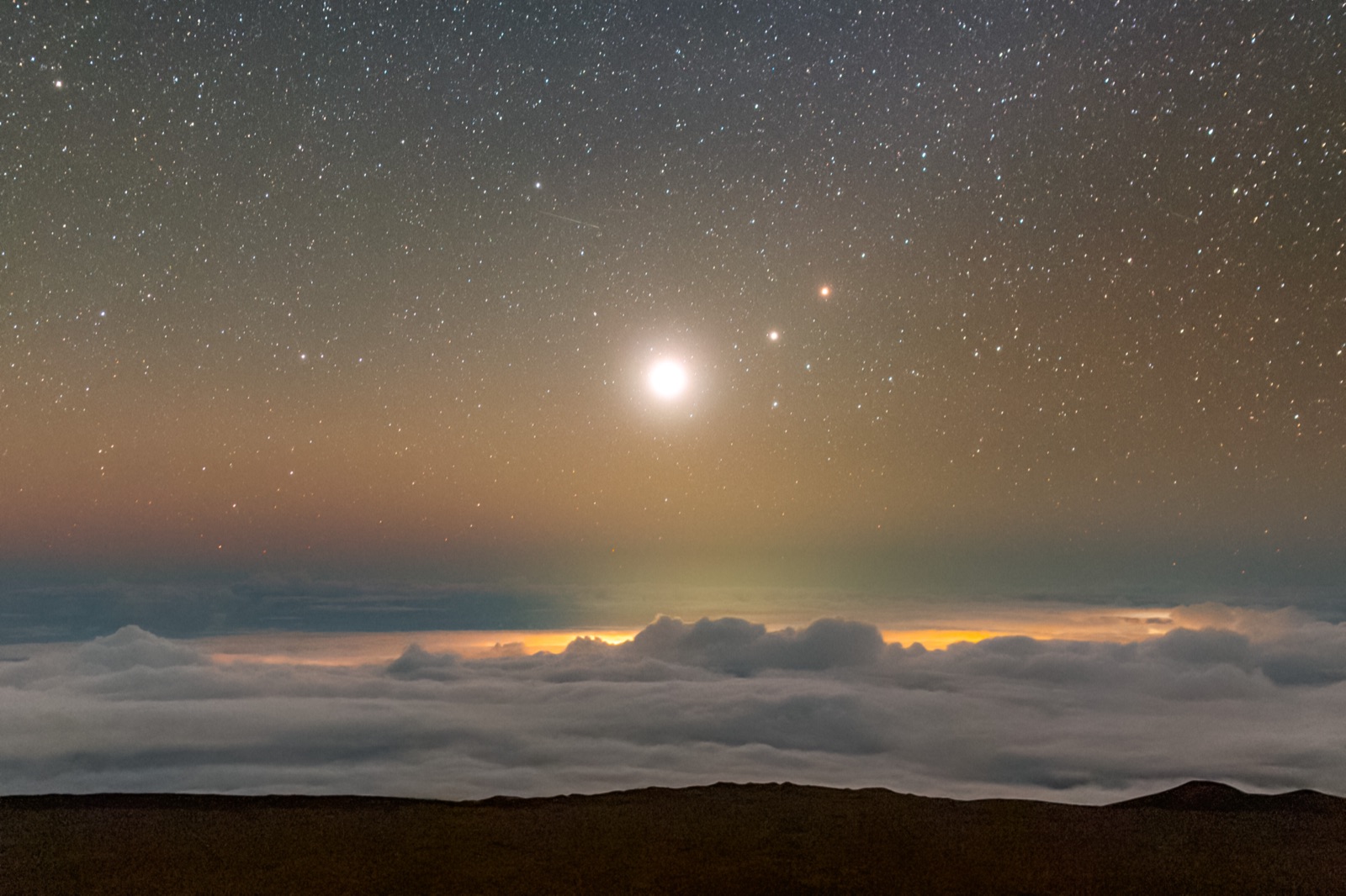 Brilliant Venus with two fainter planets in a starry pre-dawn sky above a layer of cloud.