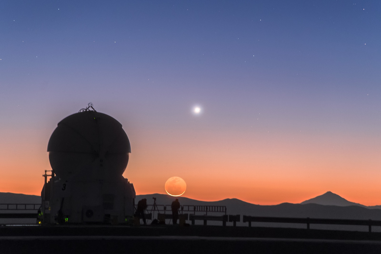 Thin crescent Moon with earthshine beside Venus in orange twilight above a telescope silhouette