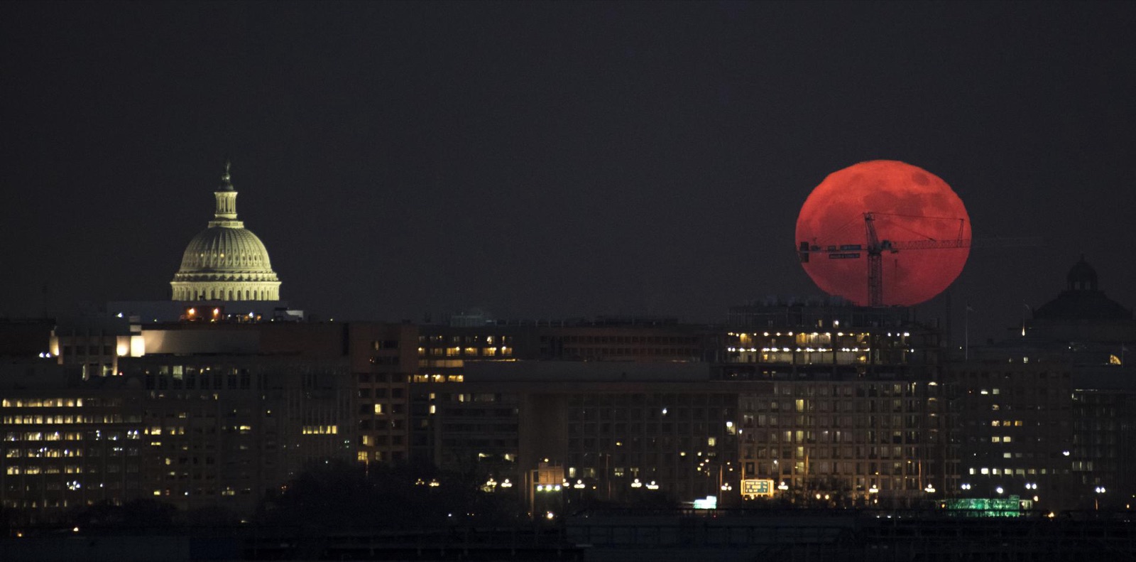 Orange full Moon low over the Washington skyline at night with the Capitol dome at left.