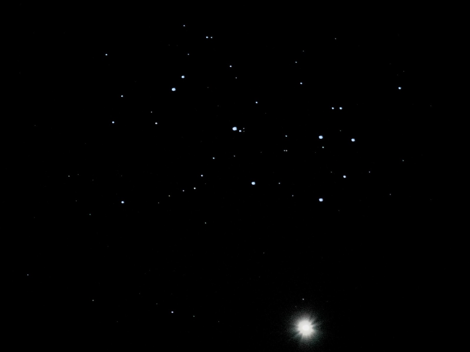 Bright overexposed Venus at the bottom of a black frame with the Pleiades star cluster above.