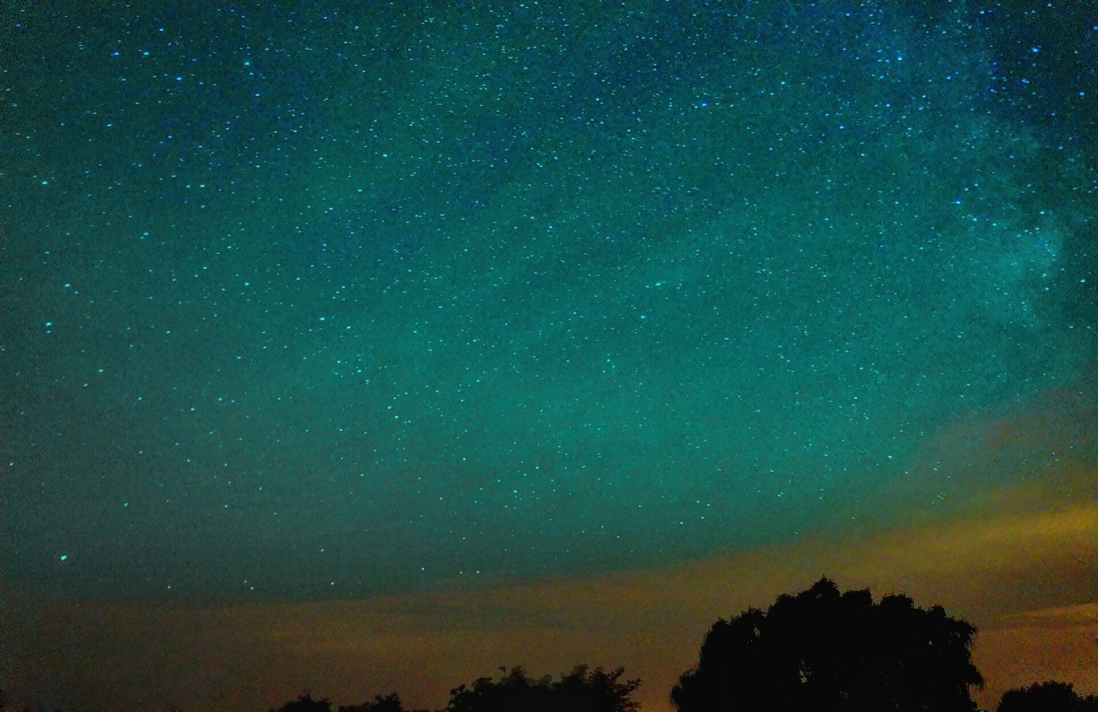 Faint green rippled airglow bands in a dark starry sky over countryside